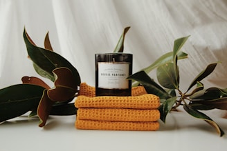 a candle sits on a stack of towels next to a plant