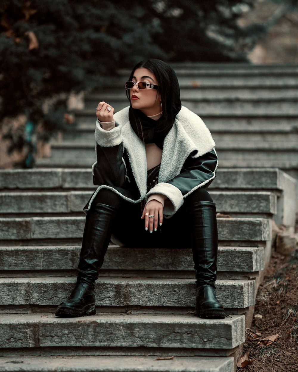 a woman sitting on some steps wearing black boots