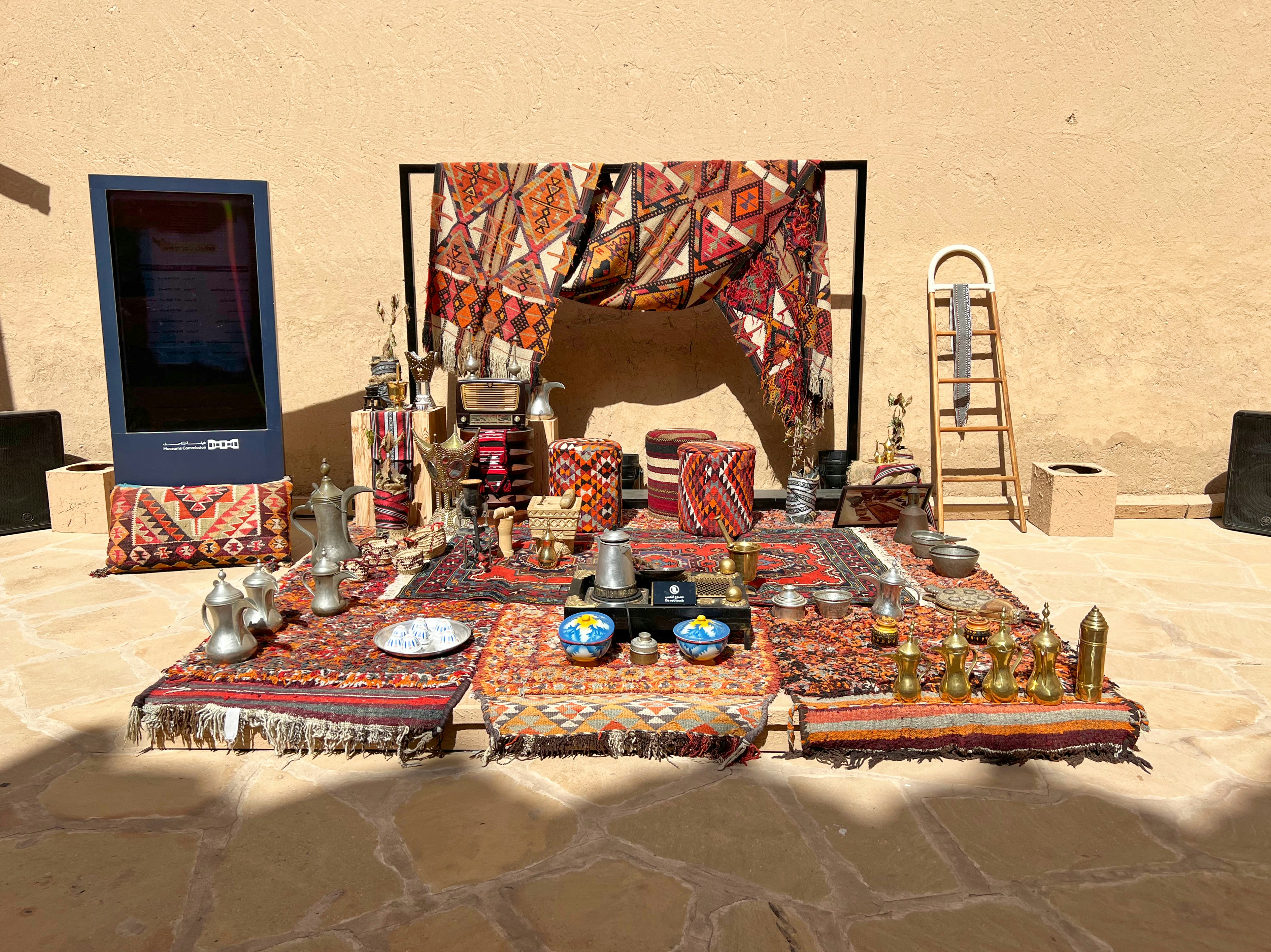 Traditional coffee pots and embroidered textiles display near an adobe wall.