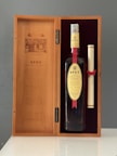 A wooden box containing a bottle of Spey single malt scotch whisky and a scroll tied with a red ribbon. The box is open, showing an inscription on the left panel and the bottle with a beige label on the right, set against a dark red velvet background.