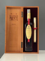 An elegant gift box open to reveal a whiskey smoker and ice stones nestled in soft amber-toned fabric.