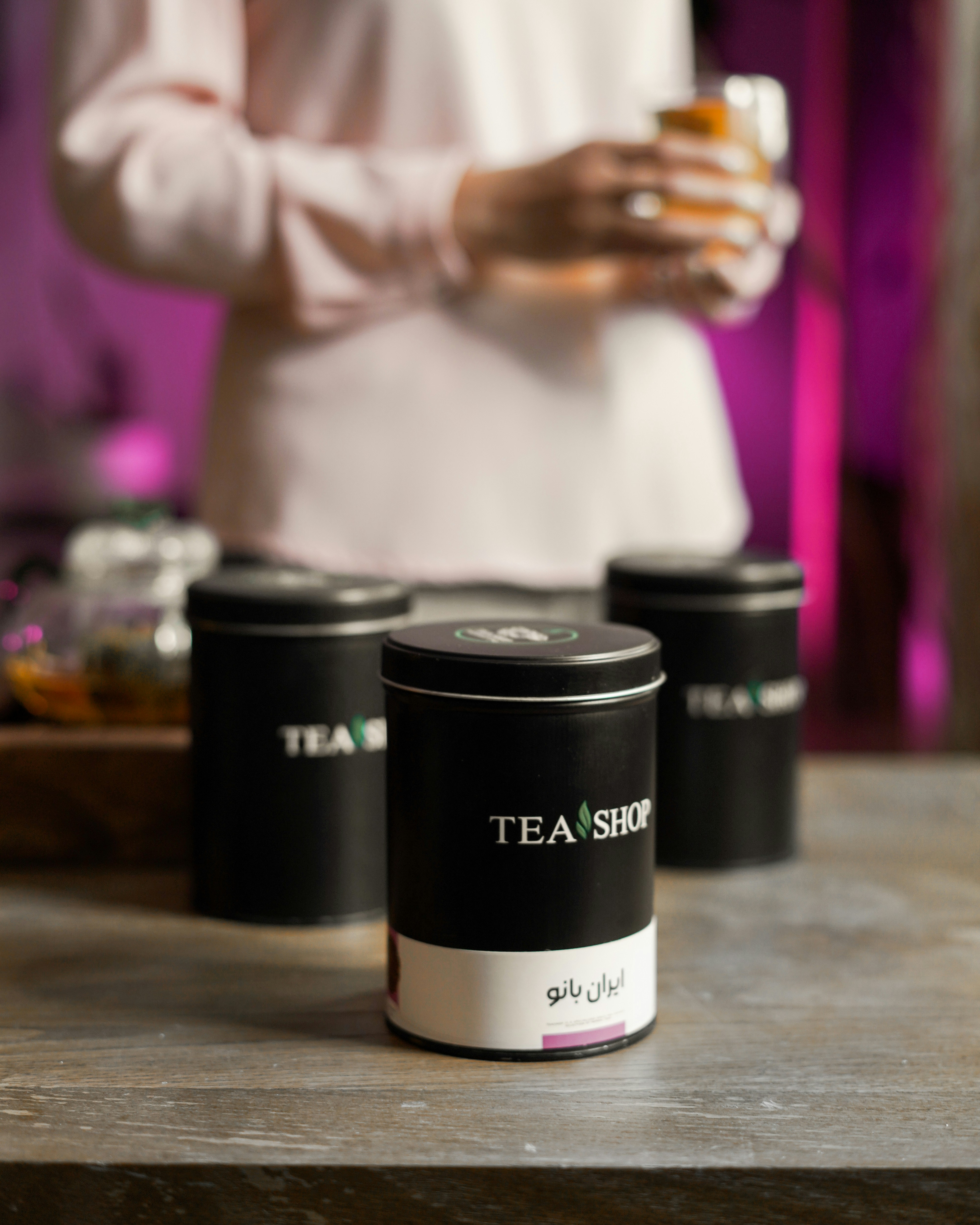 a person holding a glass of tea in front of three black canisters