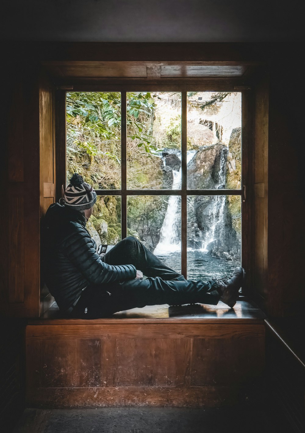 a man sitting on a window sill looking out at a waterfall