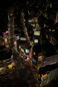 A panoramic view of several LED billboards lighting up a busy urban intersection at night.
