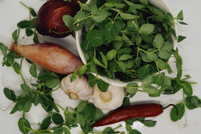 Fresh vegetables and herbs arranged next to a bottle of seh enhancer on a clean white countertop.
