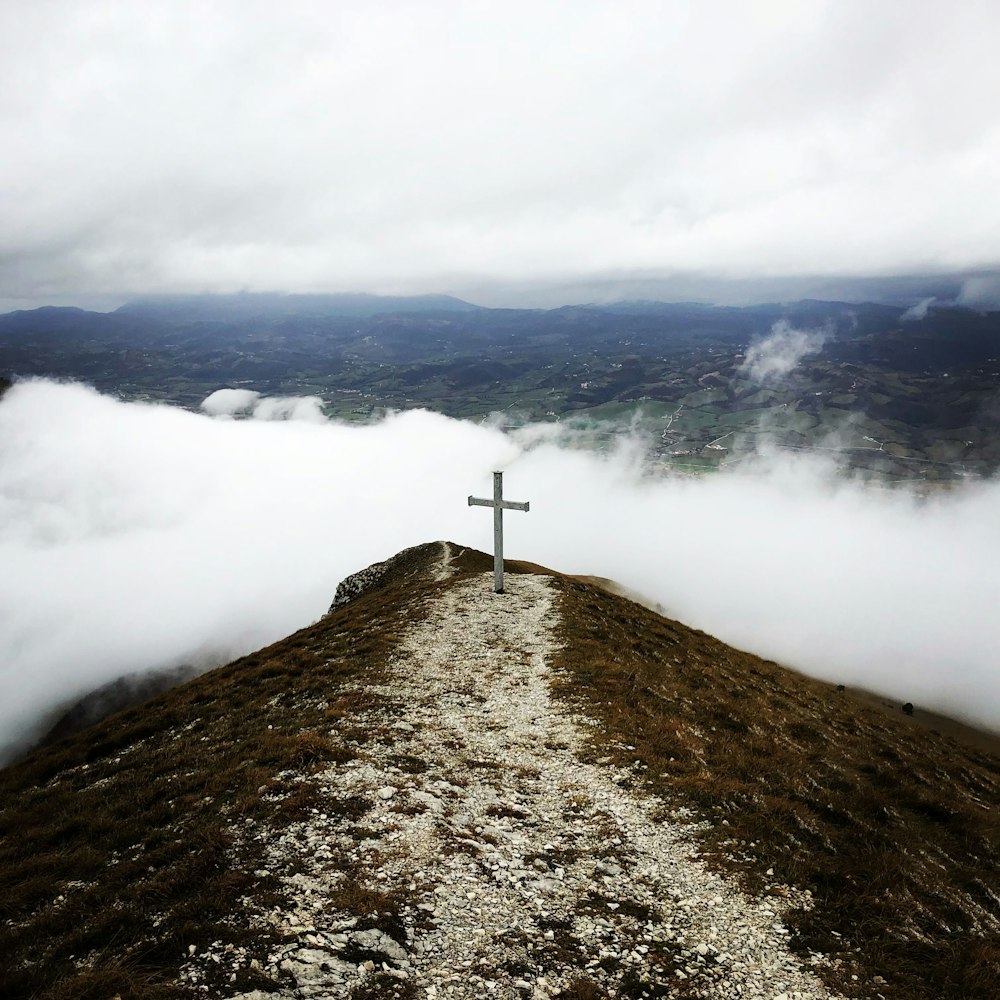 a cross sitting on top of a hill covered in clouds