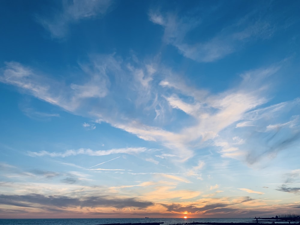 the sun is setting over the ocean with clouds in the sky