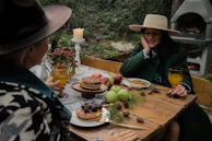 A couple enjoying breakfast outside their Rumbolibre trailer surrounded by pine trees.