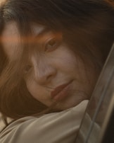 A close-up of a person's face with a serene expression, with soft lighting creating a warm ambiance. Strands of hair partially cover the face, adding to the intimate and gentle mood.