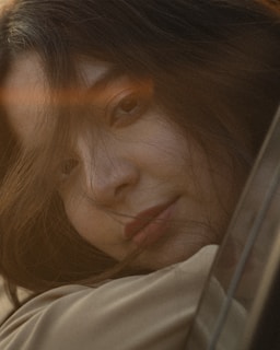 A close-up of a person's face with a serene expression, with soft lighting creating a warm ambiance. Strands of hair partially cover the face, adding to the intimate and gentle mood.