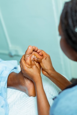A person is receiving a foot massage, with hands gently pressing on the sole of the foot. The setting appears to be a relaxing environment with a blue and white color scheme. The details of the foot and hands are clear, indicating a therapeutic or spa-like scene.