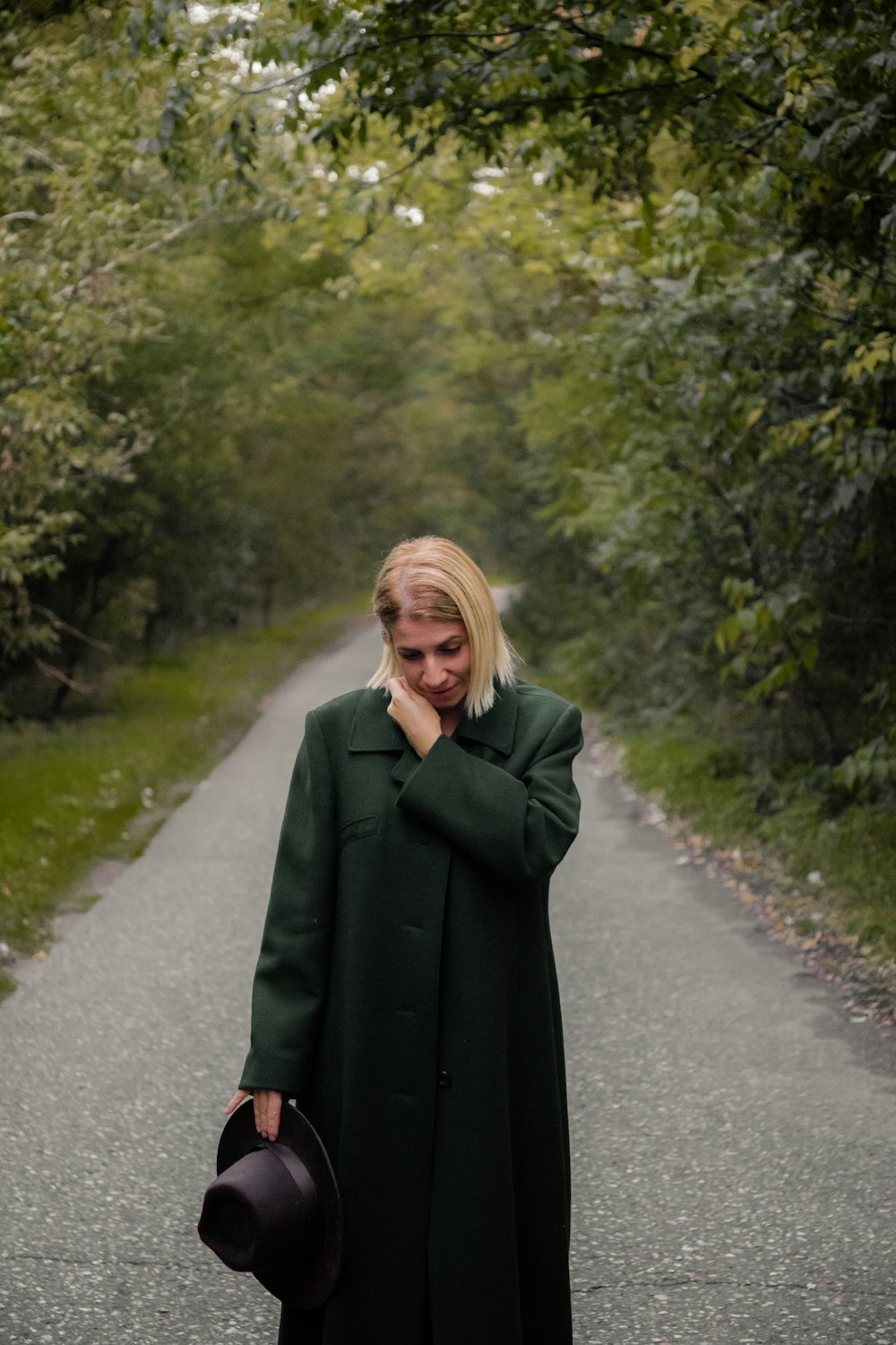 a woman in a green coat and hat walking down a road