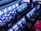 A bustling arcade filled with rows of gaming machines, each with vibrant displays and controls. Several people are seated at these machines, deeply engaged in playing games. Bright fluorescent lights cast a blue and neon glow across the room, enhancing the lively and energetic atmosphere.