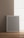 A blank gray picture frame with a white border is leaning against a beige wall on a wooden floor. Soft natural light is coming through a large window on the right, creating a calm and minimalistic atmosphere.