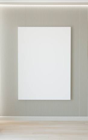 A minimalist interior featuring a large blank white canvas on a wall with vertical grooves. The floor is wooden, and there's soft lighting from above.