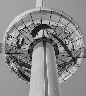 A modern observation tower with a large, circular viewing pod. The pod is reflective, showing various angles and reflections of the surrounding environment. The structure is sleek and futuristic in design.