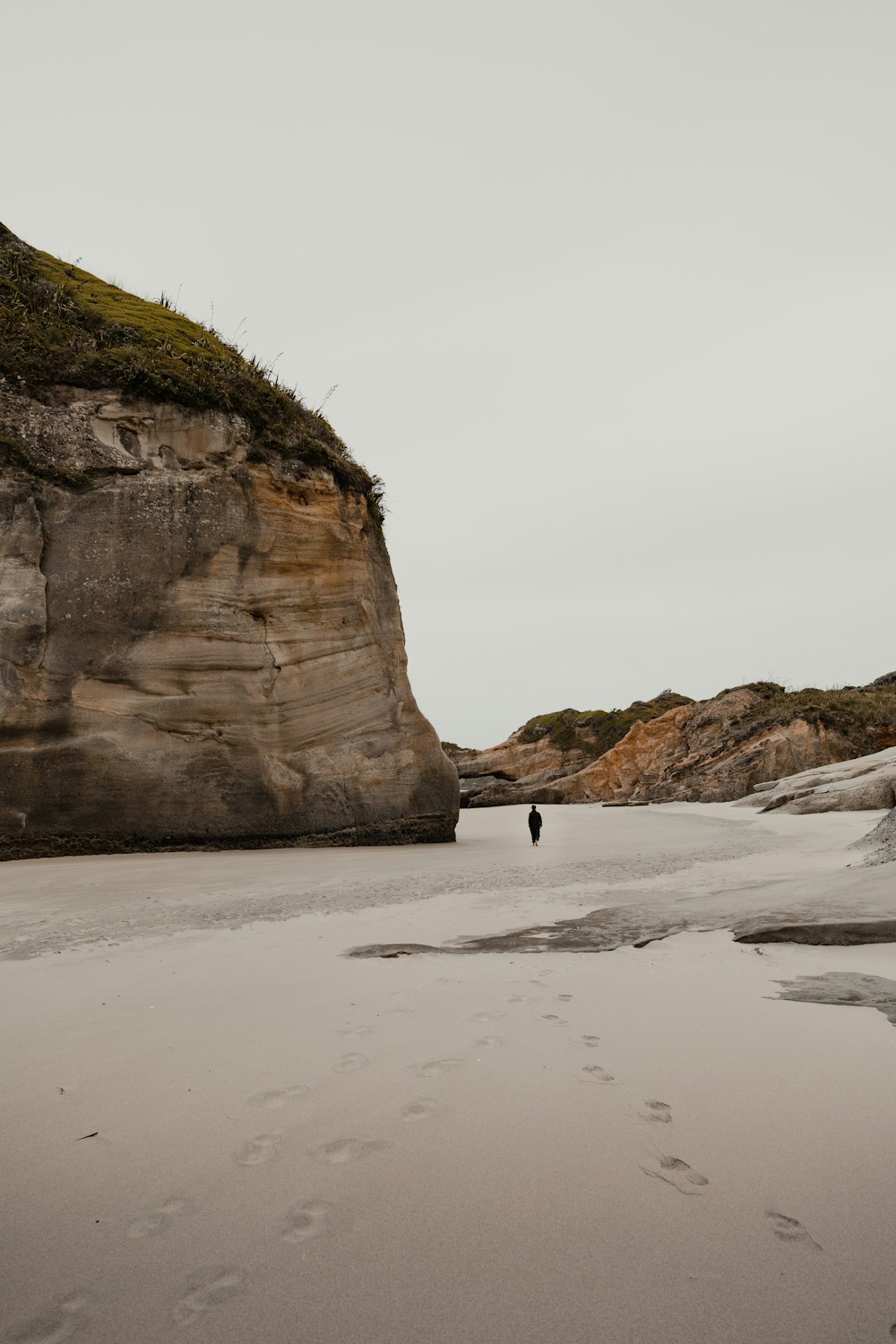 uma pessoa andando em uma praia ao lado de um penhasco