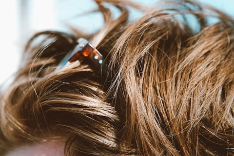 Close-up of brown hair with a tortoiseshell hair clip partially visible. The hair appears to be textured and voluminous, reflecting light.