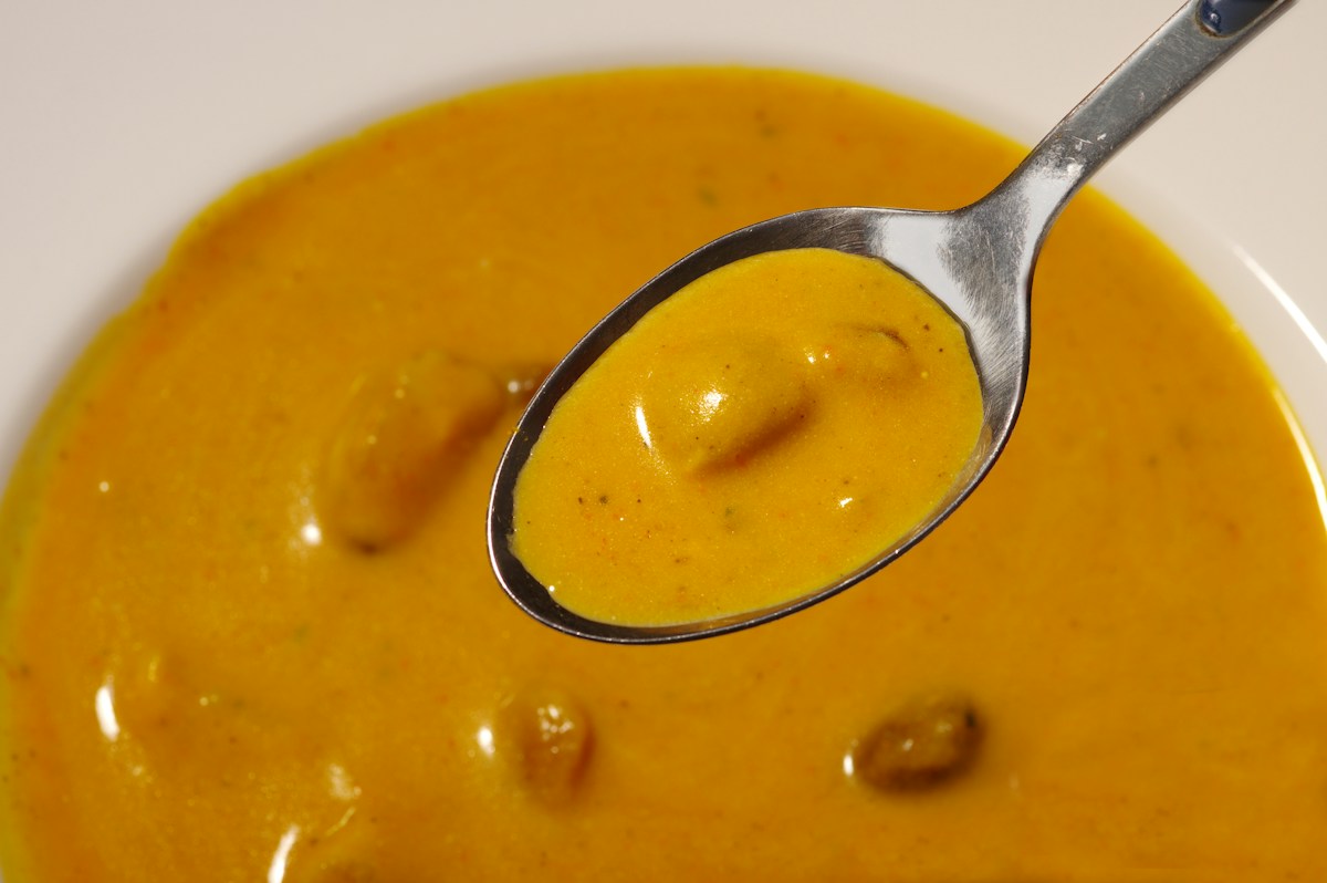 Löffel wird prüfend über einer Suppe angehoben, Abschmecken in der Küche