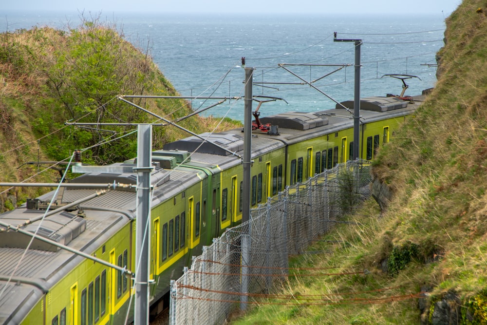 a green and yellow train traveling down tracks next to the ocean