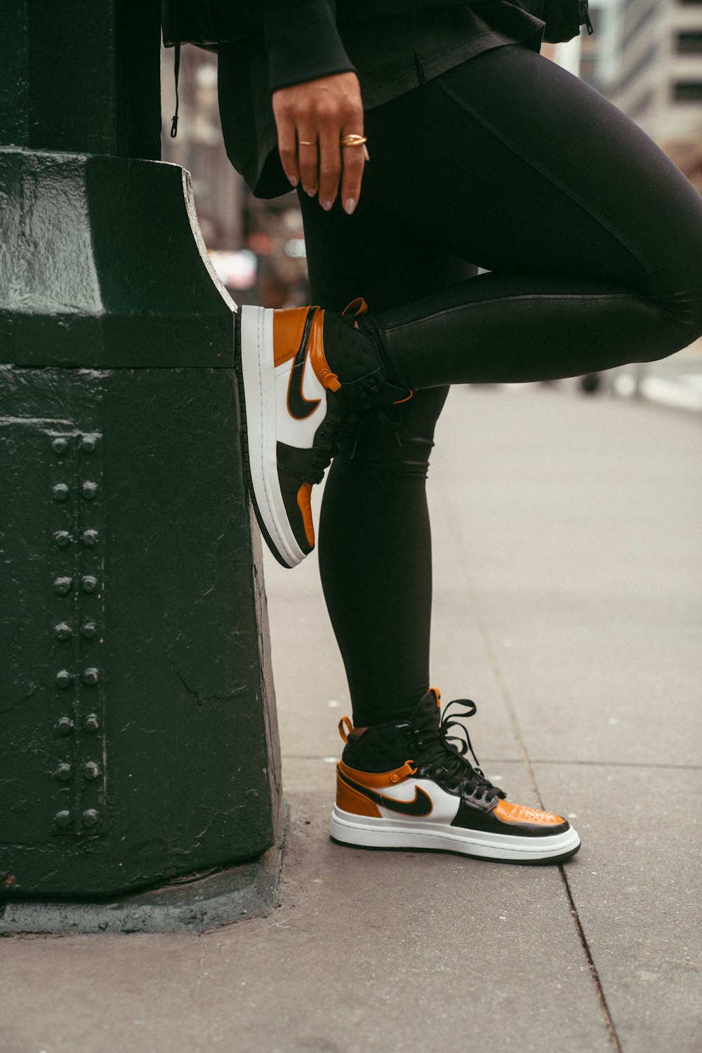 a person in black and orange sneakers leaning against a pole