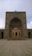 An ornate and detailed Islamic architectural structure with intricate geometric patterns and calligraphy. The colors are neutral, with a blend of light browns and blues. The entrance is arched with a pointed dome, typical of traditional mosque design.