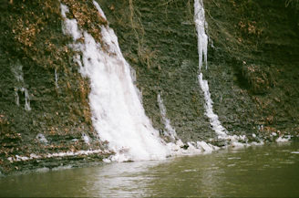 a man standing in the water next to a waterfall