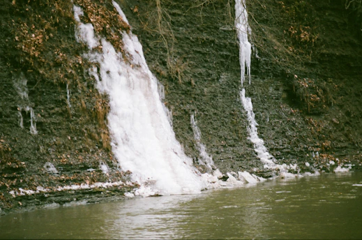 a man standing in the water next to a waterfall