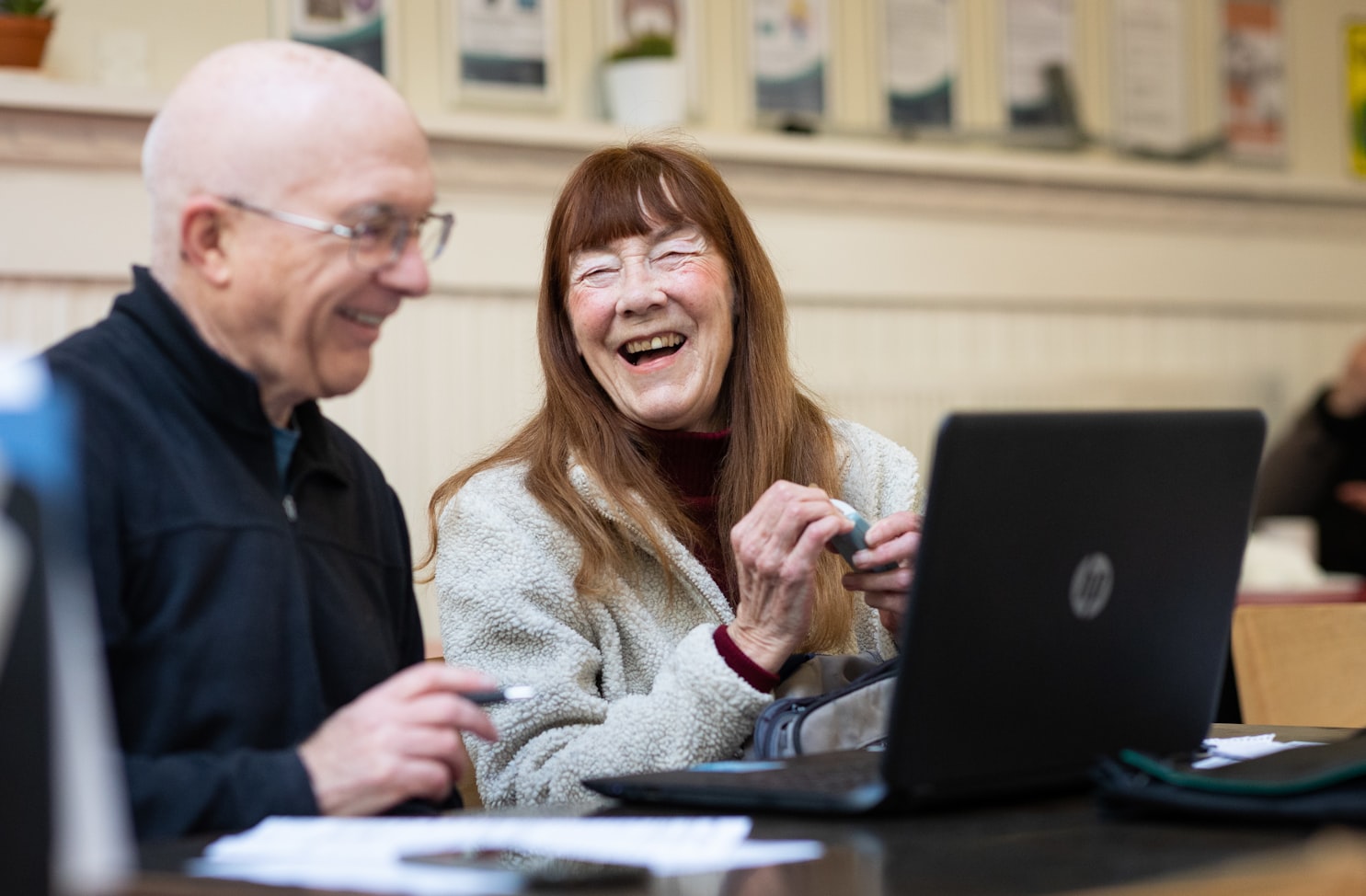 An older man and woman are laughing while using a laptop