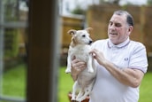 Smiling pet owner holding a freshly groomed small dog outside their house.
