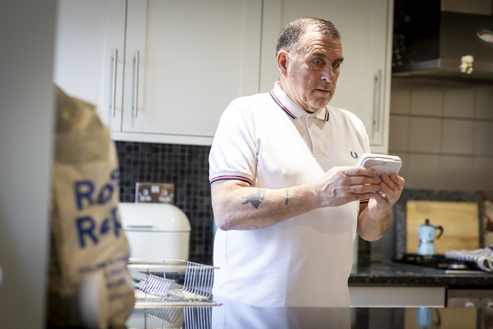 a man standing in a kitchen looking at a cell phone