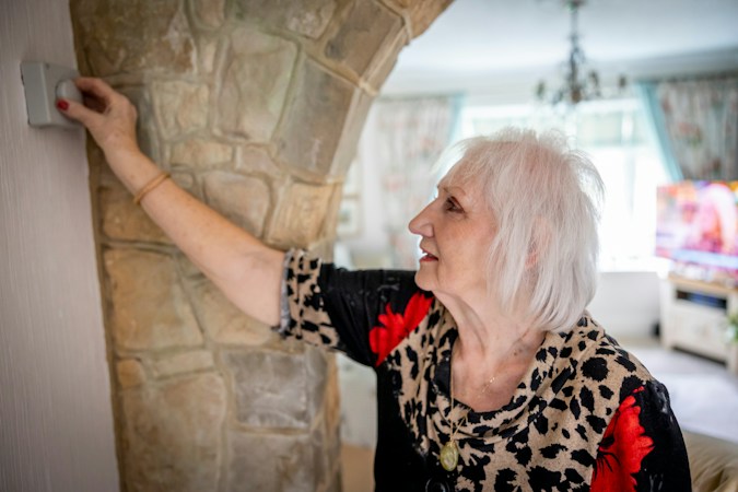 An older woman at home adjusting a wall switch, a reminder to check that older neighbors in Clark County have working cooling during heat