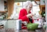 A smiling elderly woman holding a grocery bag in a cozy kitchen.