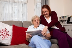 a woman sitting on a couch next to a woman reading a newspaper