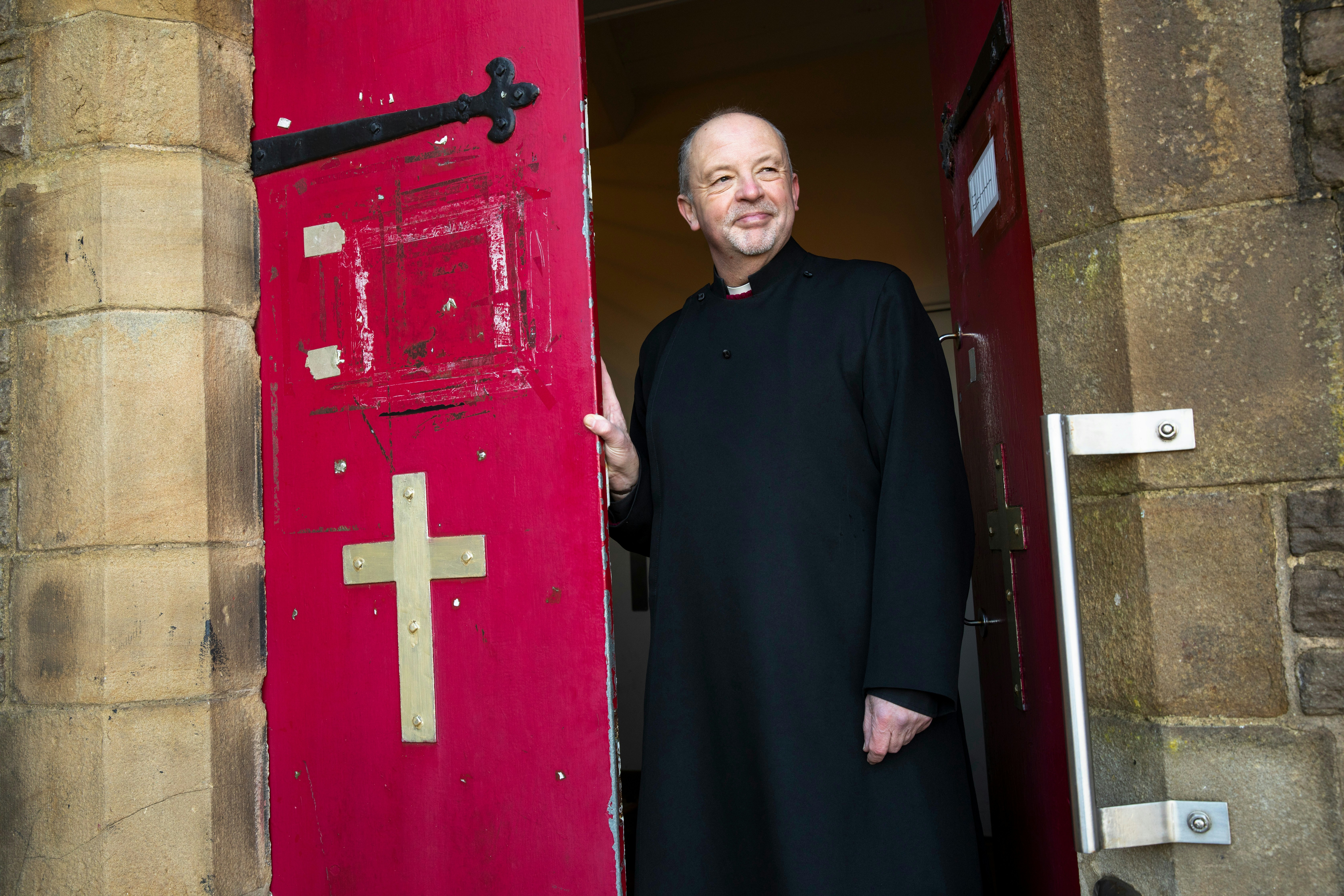 Clergyman smiling while holding open a church door.