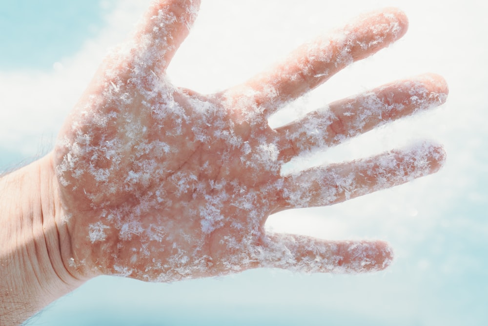 a person's hand covered in snow against a blue sky
