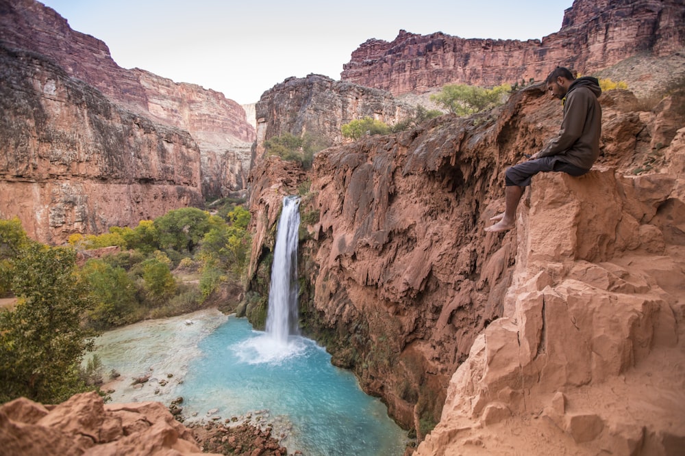 a man sitting on a cliff next to a waterfall