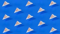 A pattern of small triangular packages, each with a coin featuring a pound symbol, is arranged uniformly across a bright blue background. The design is minimalistic and modern, featuring clean lines and a stark contrast between the blue and the white of the packages.
