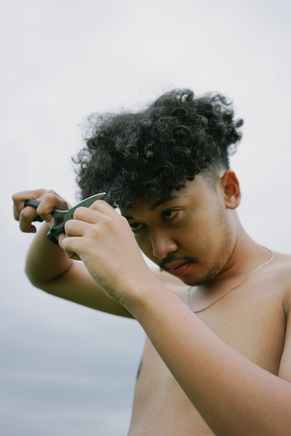 a shirtless man is cutting his hair with scissors