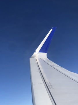 The image features the wing of an airplane, with a clear sky in the background. The wing has a prominent upward curve, and the upper part of the winglet is painted blue. The clean and streamlined design highlights the aircraft's engineering.