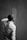 A person is seen from behind as they paint a wall. They are wearing a long-sleeved shirt and appear to be focused on applying paint evenly across the surface. The image is in black and white, emphasizing contrast and texture.