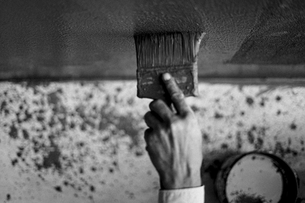 a person holding a paint brush in front of a dirty wall