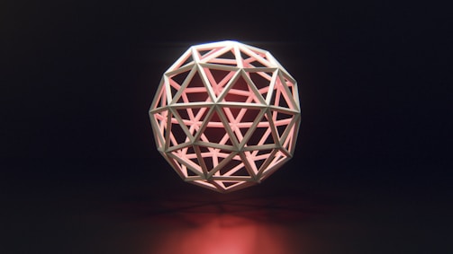 A geometric sphere composed of triangular and polygonal shapes is intricately arranged in a symmetrical pattern. The structure emits a soft pink glow from within, casting subtle reflections on a dark background.