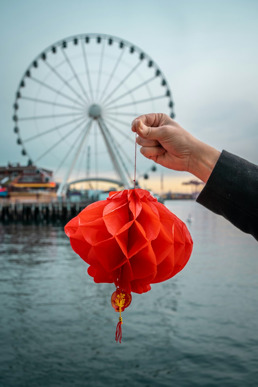 a person holding a red paper lantern in front of a ferris wheel