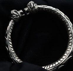 An elegant silver bracelet with intricate detailing displayed on a velvet cushion.