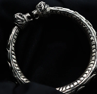 A stylish bracelet with intricate metalwork displayed on a velvet cushion.