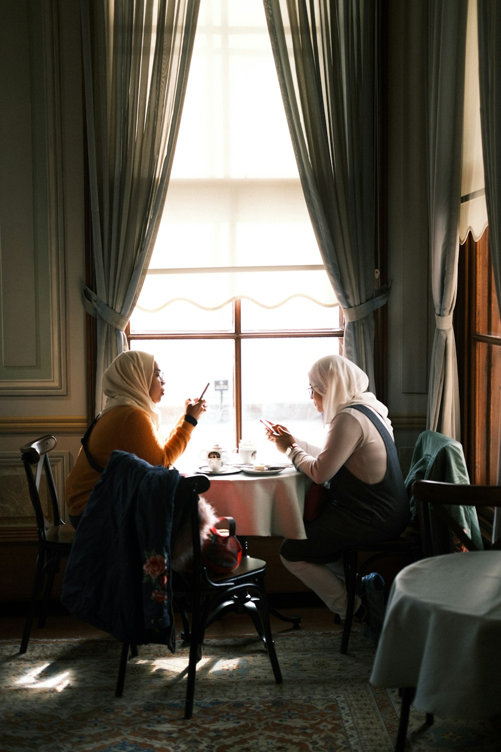 two women sitting at a table in front of a window