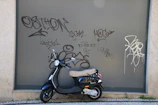A compact scooter parked beside a city street with vibrant urban graffiti.