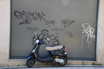 A compact scooter parked beside a city street with vibrant urban graffiti.