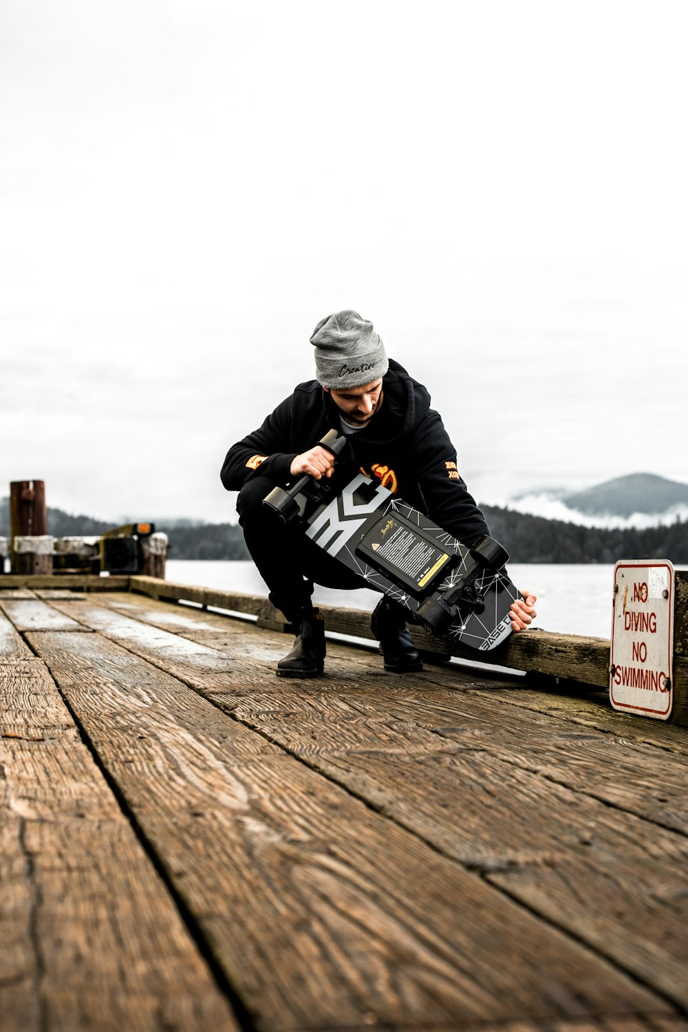 a man holding a skateboard on top of a wooden pier